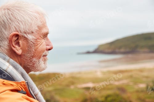 Preview: Profile Shot Of Active Senior Man Walking Along Coastal Path In Winter With Beach And Cliffs Behind