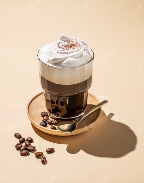 Preview: Iced coffee in a glass with foam on a yellow background with coffee beans and morning shadows.