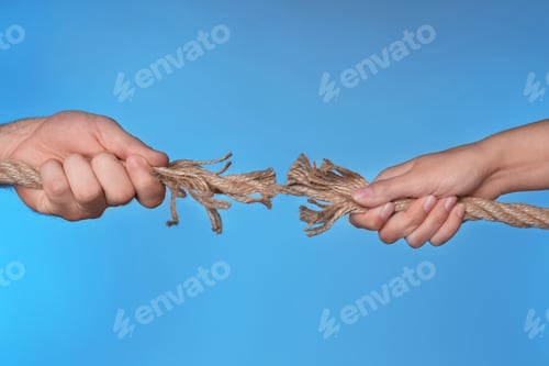 Preview: Woman and man pulling damaged rope on color background, closeup