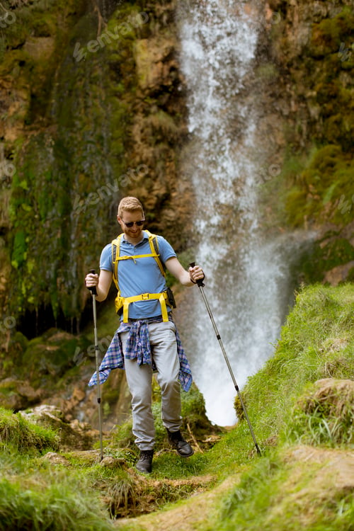 Preview: Young hiker stopped beside a mountain waterfall to rest