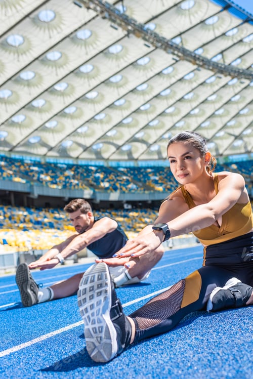 Preview: young attractive couple sitting on running track and stretching at sports stadium