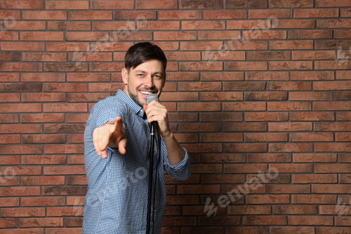 Preview: Handsome man in shirt singing with microphone near brick wall. Space for text