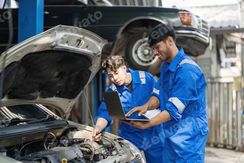 Preview: Young Man Repairing Car at Auto Repair Shop with Mechanic Using Laptop for Diagnostics in