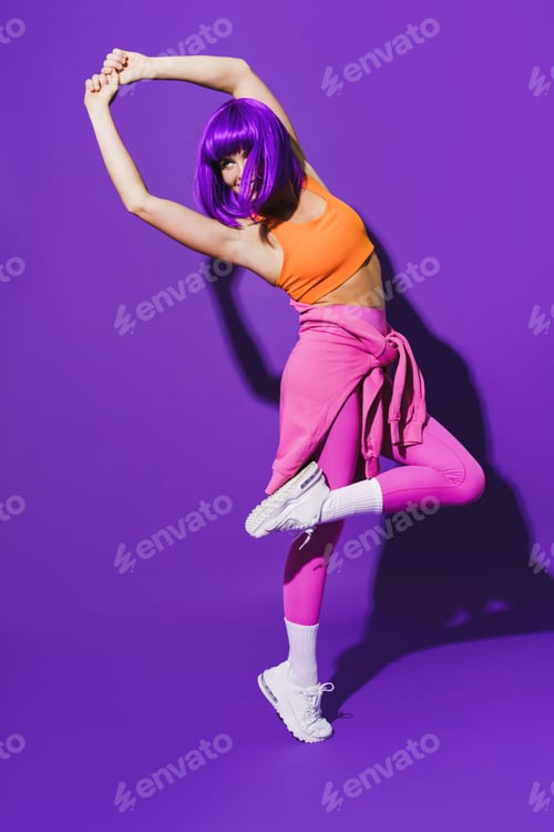 Preview: Carefree woman dancer wearing colorful sportswear performing against purple background