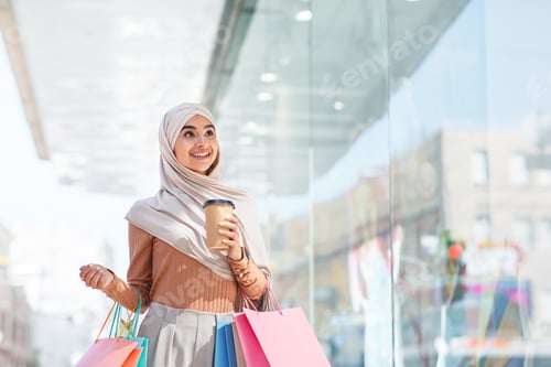 Preview: Inspired happy emotional cute millennial middle eastern lady in hijab with many packages and cup of