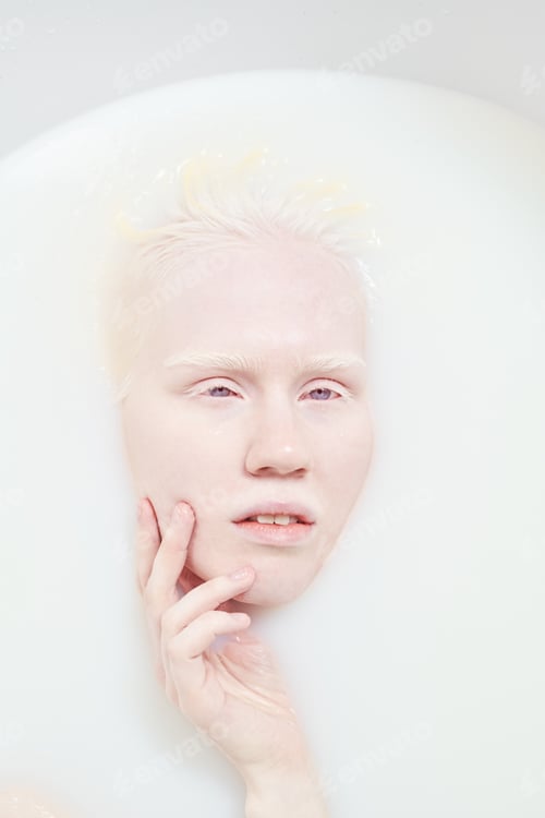 Preview: Serene albino woman with no makeup on her face lying in bathtub with milk