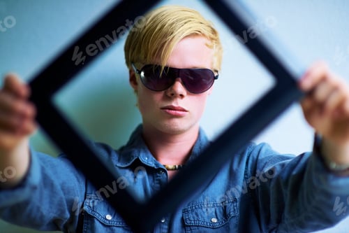 Preview: Staying in the frame. Trendy young guy holding up a frame that frames his face.