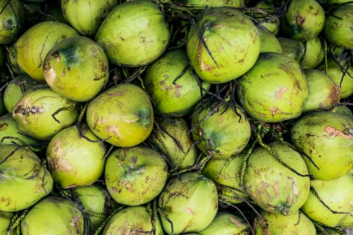 Preview: High angle close up of green coconuts piled high at a street side market.