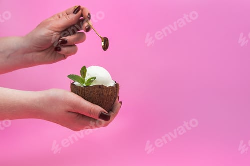 Preview: Vanilla ice cream balls in a fresh coconut half, decorated with mint leaves in the hand with a spoon