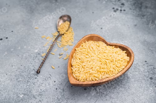 Preview: Raw Orzo pasta, uncooked dry Italian risoni in a bowl. grey background. top view