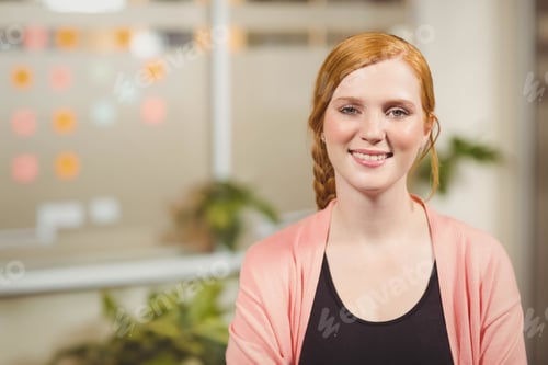 Preview: Sitting at desk, woman with red braids wearing coral cardigan near sticky notes and potted plants