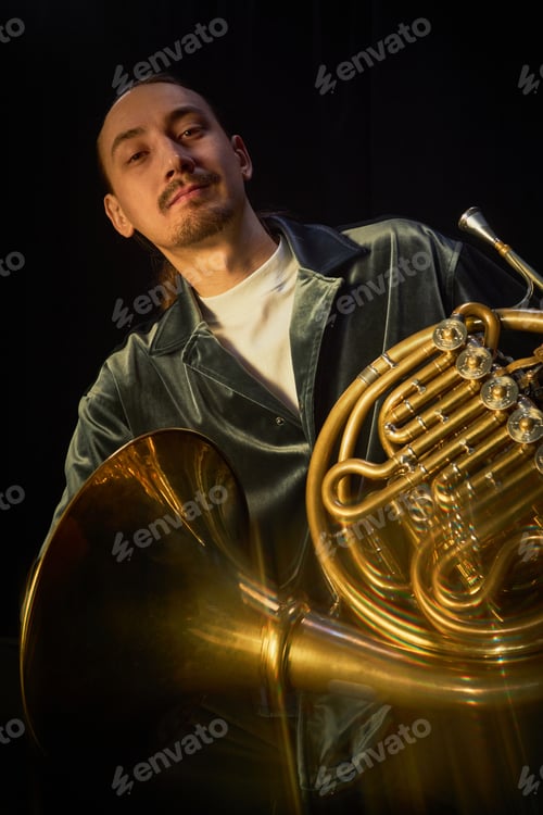 Preview: Portrait of Smiling Male Jazz Player Posing with French Horn in Studio