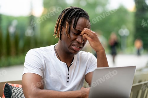 Preview: a stressed and exhausted man doing some work on his laptop outdoors