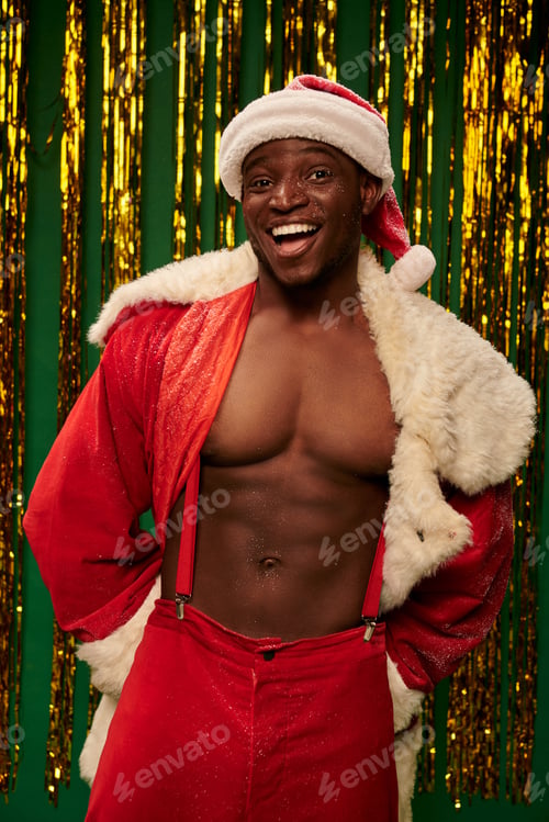 Preview: sexy sportive african american man in santa costume on shirtless body near golden tinsel on green