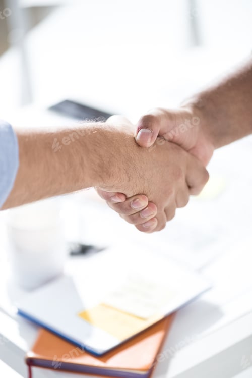 Preview: Top view of businessmen shaking hands above table with papers, business teamwork concept