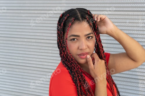 Preview: Young latin woman posing with red and black braids in front of metal wall