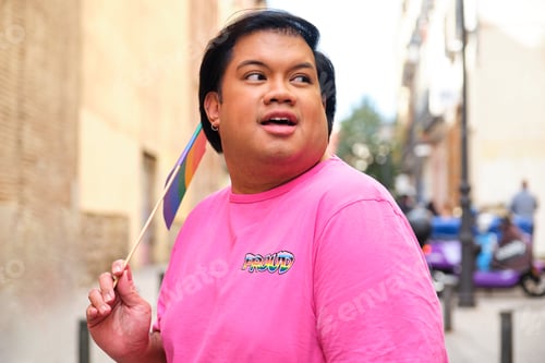 Preview: Gay Asian wearing a pink shirt holding a rainbow flag.