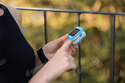 Preview: Woman checking pulse with blood pressure monitor on finger after training outdoors, closeup