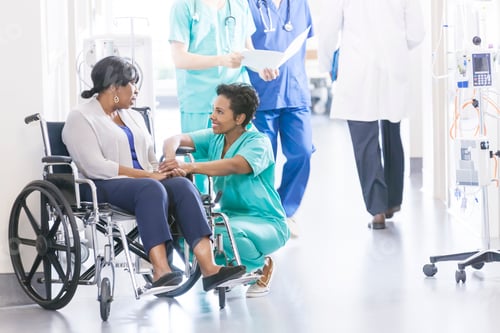 Preview: African American patient and nurse with medical staff in hospital corridor