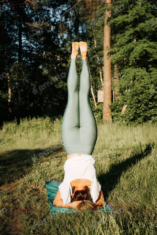 Preview: Slim athletic young woman practicing yoga asana, headstand. Rear view of a girl standing on her head