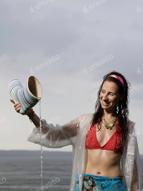 Preview: Joyful woman enjoying the rain, tipping water from a boot