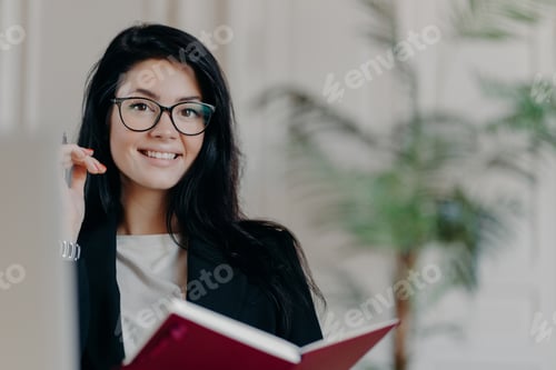 Preview: Cheerful businesswoman with glasses taking notes and smiling confidently.