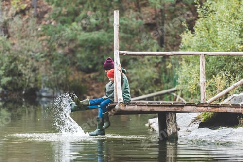 Preview: father and son sitting on wooden bridge together near lake