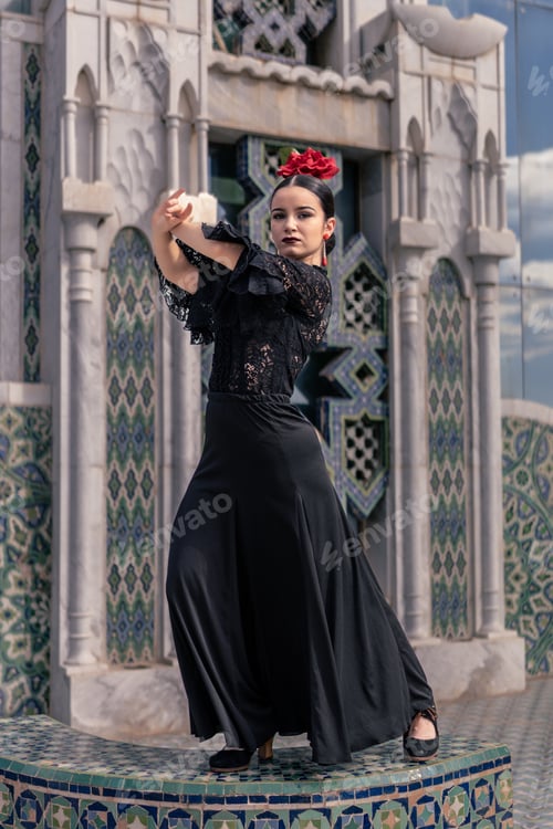 Preview: spanish young flamenco dancer dressed in black with a red rose in her hair poses on a tiled platform