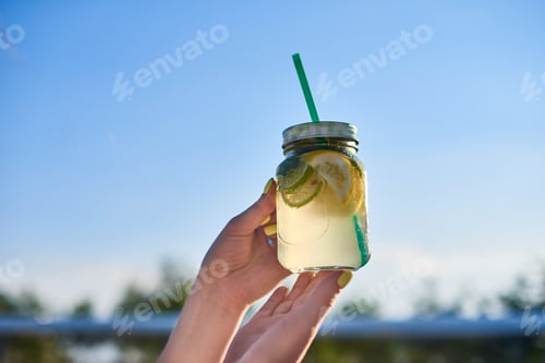 Visualização: Dieta. Alimentação saudável. Mão de mulher segurando bebida de limonada no fundo do céu azul natureza turva