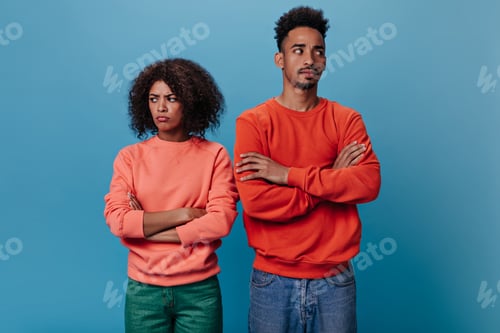 Preview: Man and woman in bad humor posing on isolated background. Portrait of sad curly girl in orange swea