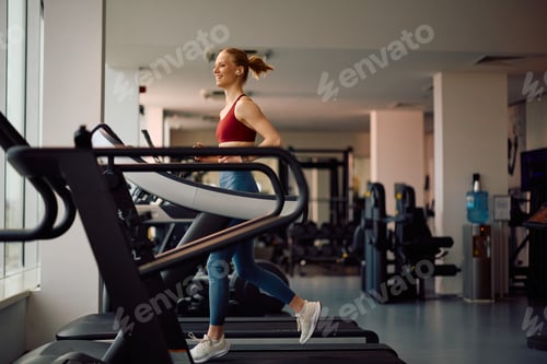 Preview: Happy female athlete exercising on running track during sports training at health club.