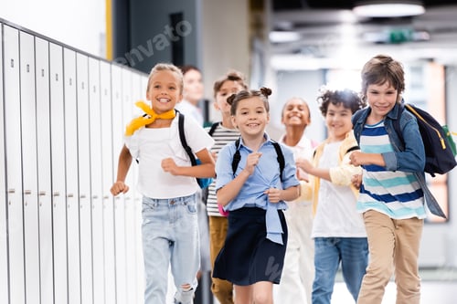 Preview: selective focus of excited multicultural classmates with backpacks running along school corridor