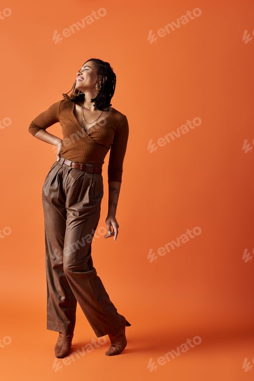 Preview: Young African American woman with braids poses in a vibrant orange studio