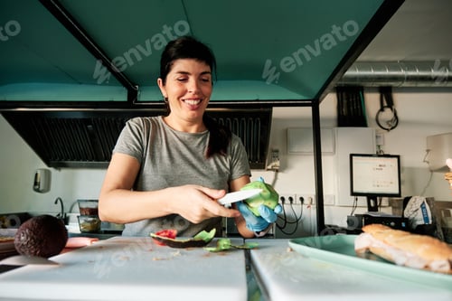 Preview: Smiling woman cutting an avocado while working in the kitchen of a health food restaurant.