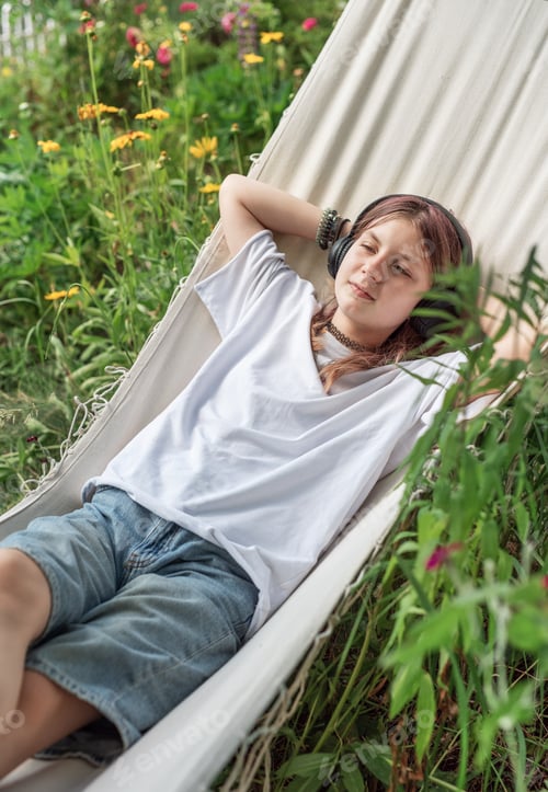 Preview: Teenage girl relaxing in hammock listening to music in garden