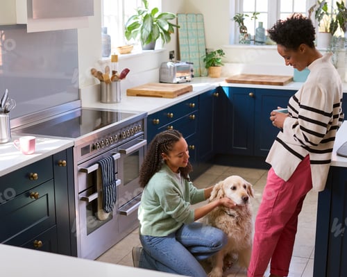 Preview: Mother Talking With Teenage Daughter Relaxing At Home In Kitchen With Pet Dog