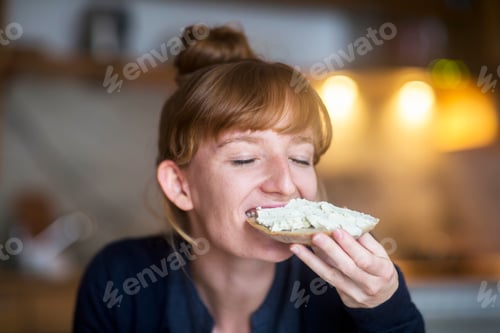 Preview: Young woman eating bread with cream cheese