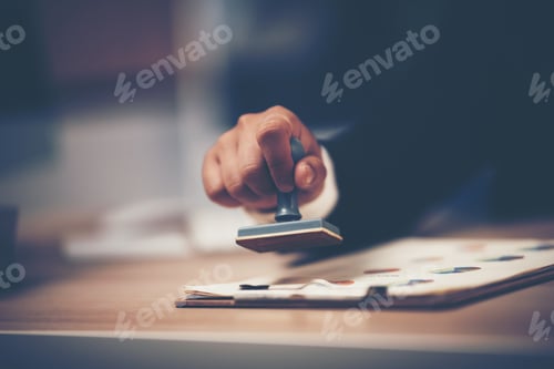 Preview: Close-up Of A Person's Hand Stamping With Approved Stamp On Document At Desk