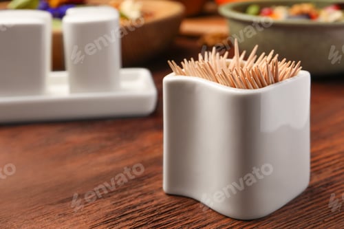 Preview: Holder with many toothpicks on wooden table, closeup. Space for text