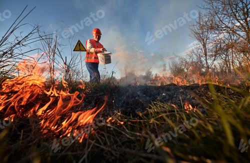 Preview: Fireman ecologist fighting fire in field in the evening