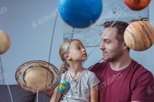 Preview: Father and daughter sitting near model of the solar system