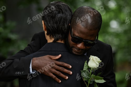 Preview: Black Man in Comforting Embrace of Woman Grieving at Cemetery