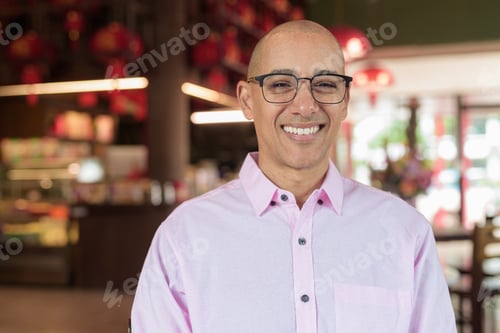 Preview: Bald Hispanic man wearing pink casual business shirt and eyeglasses in Chinese style tea house