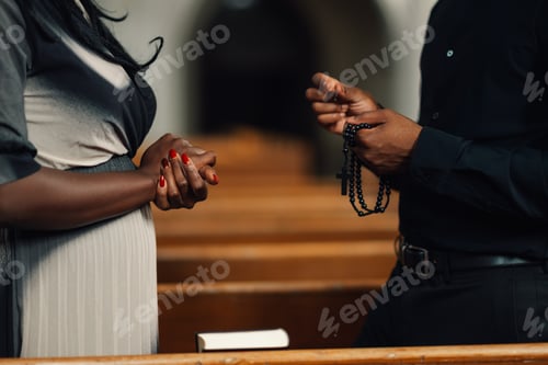 Preview: Priest holding rosary praying with churchgoer in church pews
