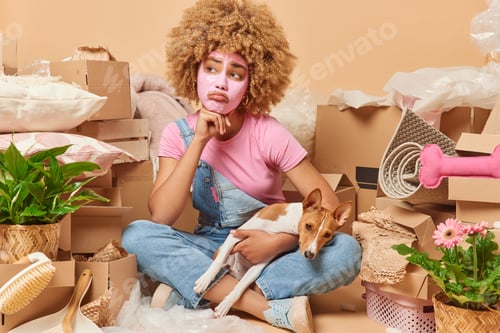 Preview: Sad unhappy woman sits in lotus pose with pedigree dog applies facial beauty mask has thoughtful exp