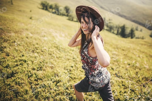 Preview: Stylish hipster girl in hat traveling on top of sunny mountains