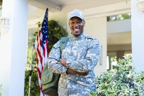 Preview: Happy african american male soldier with arms crossed in cap outside home with usa flag, copy space
