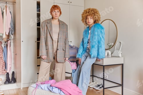 Preview: Indoor shot of two fashionable young women sort out wardrobe choose clothes for donation pose in