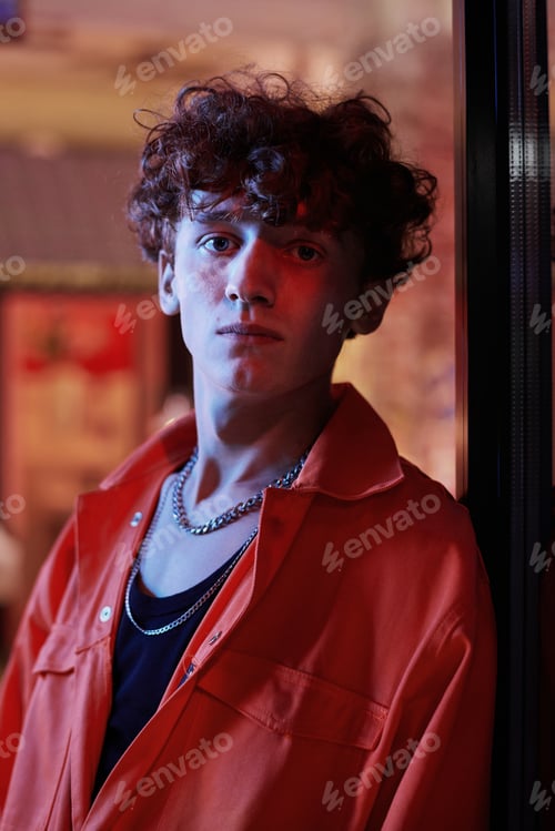 Preview: Curly guy in trendy orange bomber jacket and black singlet looking at camera