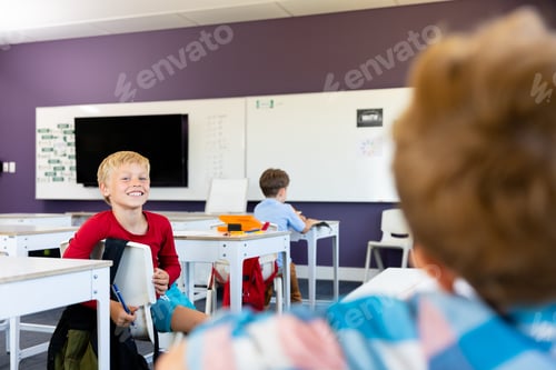 Preview: Caucasian elementary schoolboys talking while sitting at desk in school